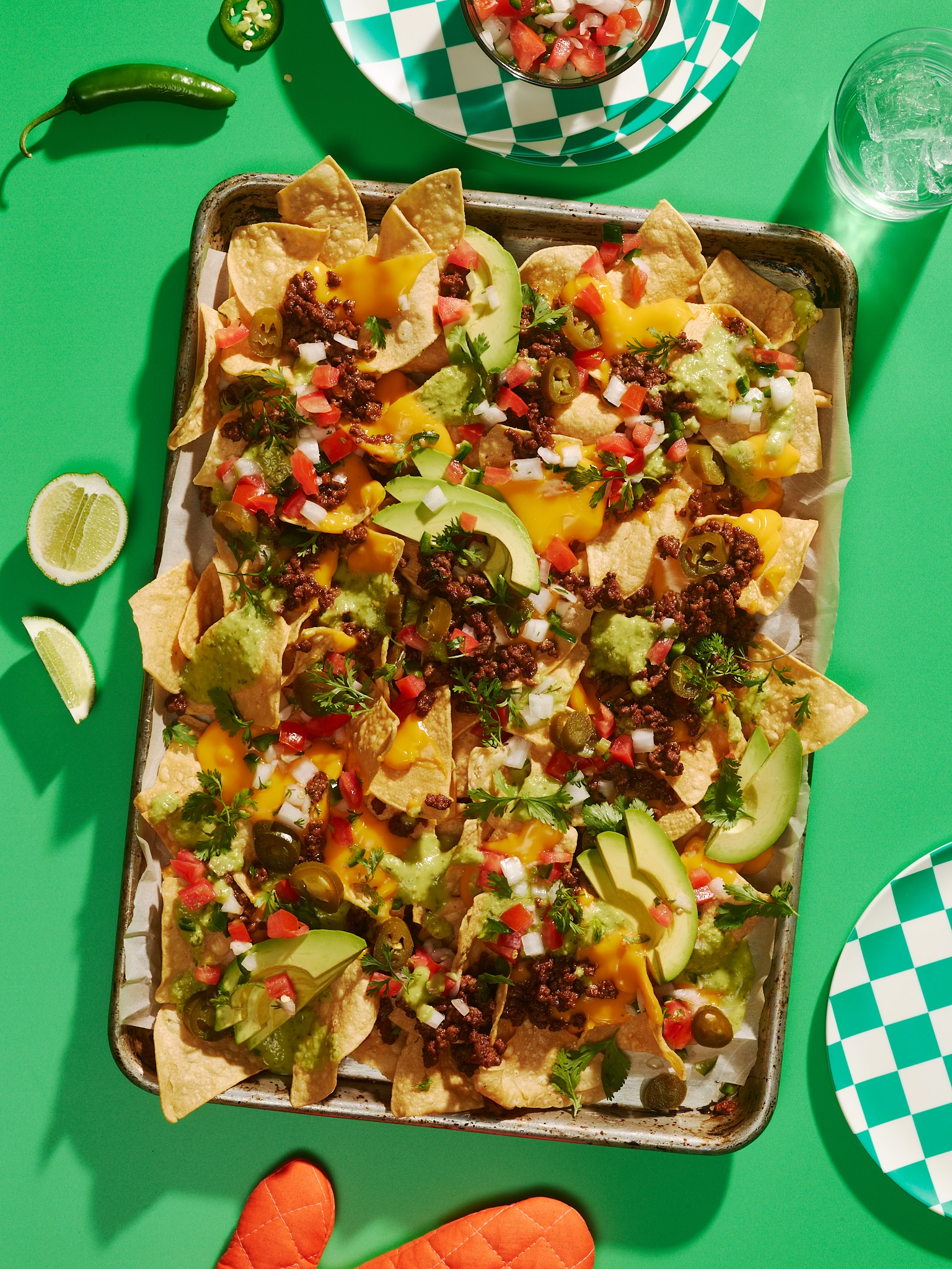 Overhead shot of fully loaded nachos on a baking sheet, featuring tortilla chips, melted cheese, salsa, guacamole, and jalapenos.
