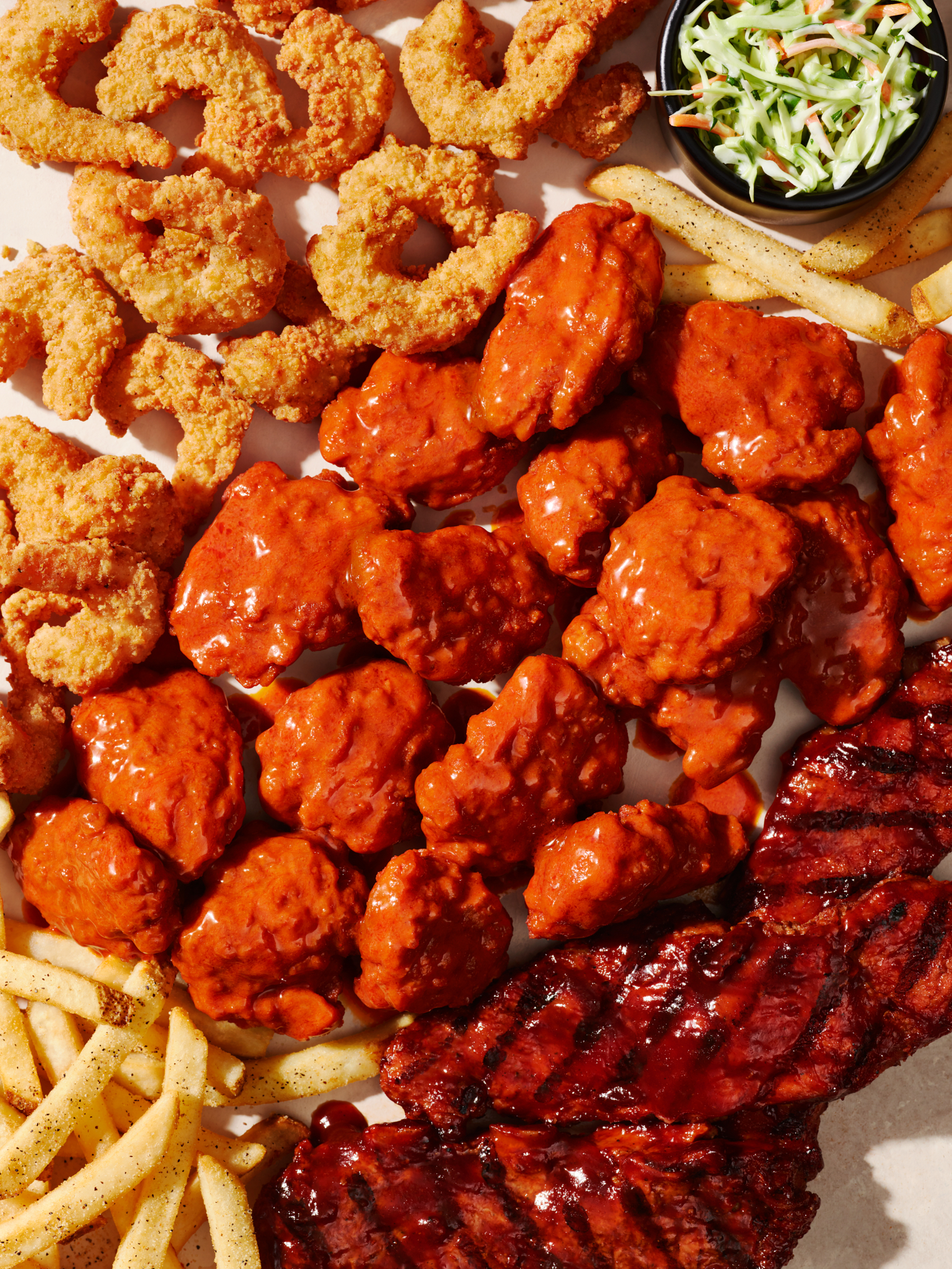 Overhead shot of fried shrimp, chicken wings, ribs, french fries, and coleslaw on a white surface, showcasing a variety of foods.