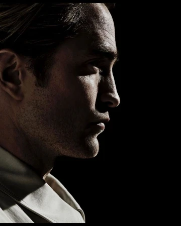 Dramatic portrait of a man in profile with strong lighting, showcasing his facial features against a stark black backdrop, wearing a light-colored shirt.