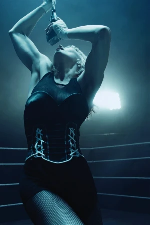 A blonde woman in a black top and lace-up corset holds a microphone in a boxing ring under dramatic lighting.