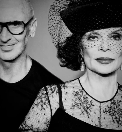 Black and white portrait of a woman in a netted hat and lace top next to a man wearing glasses, photographed by Tom Munro
