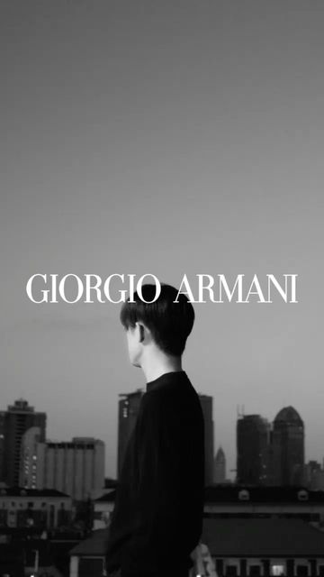 Black-and-white shot of a person looking at city buildings under a twilight sky, with 'GIORGIO ARMANI' text overlay.