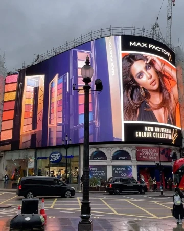 Max Factor advertisement on a large digital billboard in London's Piccadilly Circus, featuring cosmetics and a model's face.