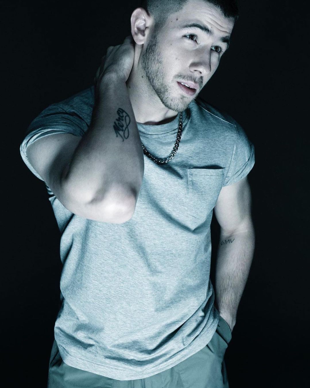 Portrait of a young adult man with short dark hair and a gray t-shirt, posing indoors in a dark, intimate setting.