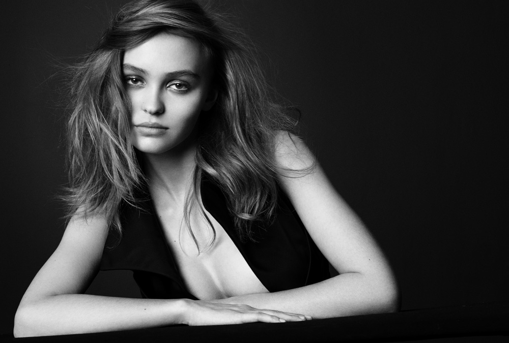 Monochrome portrait of Lily-Rose Depp leaning forward with tousled hair against a dark studio background