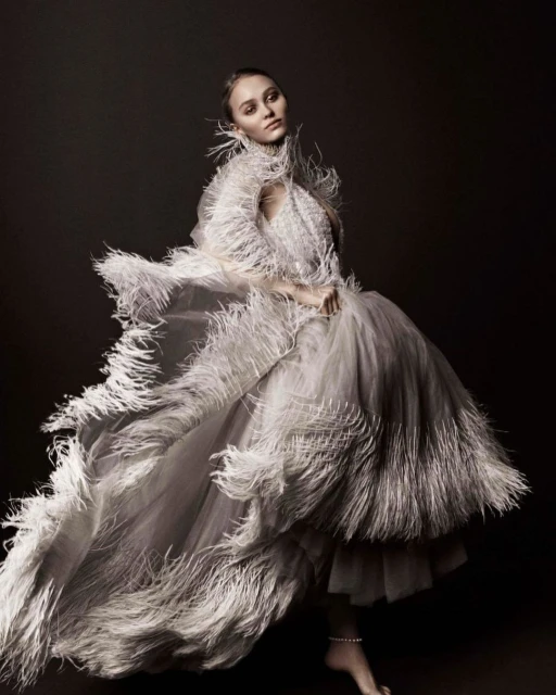 Elegant woman in an elaborate white feathered gown strikes a pose in a studio, creating a visually striking fashion portrait.
