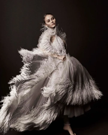 Elegant woman in an elaborate white feathered gown strikes a pose in a studio, creating a visually striking fashion portrait.