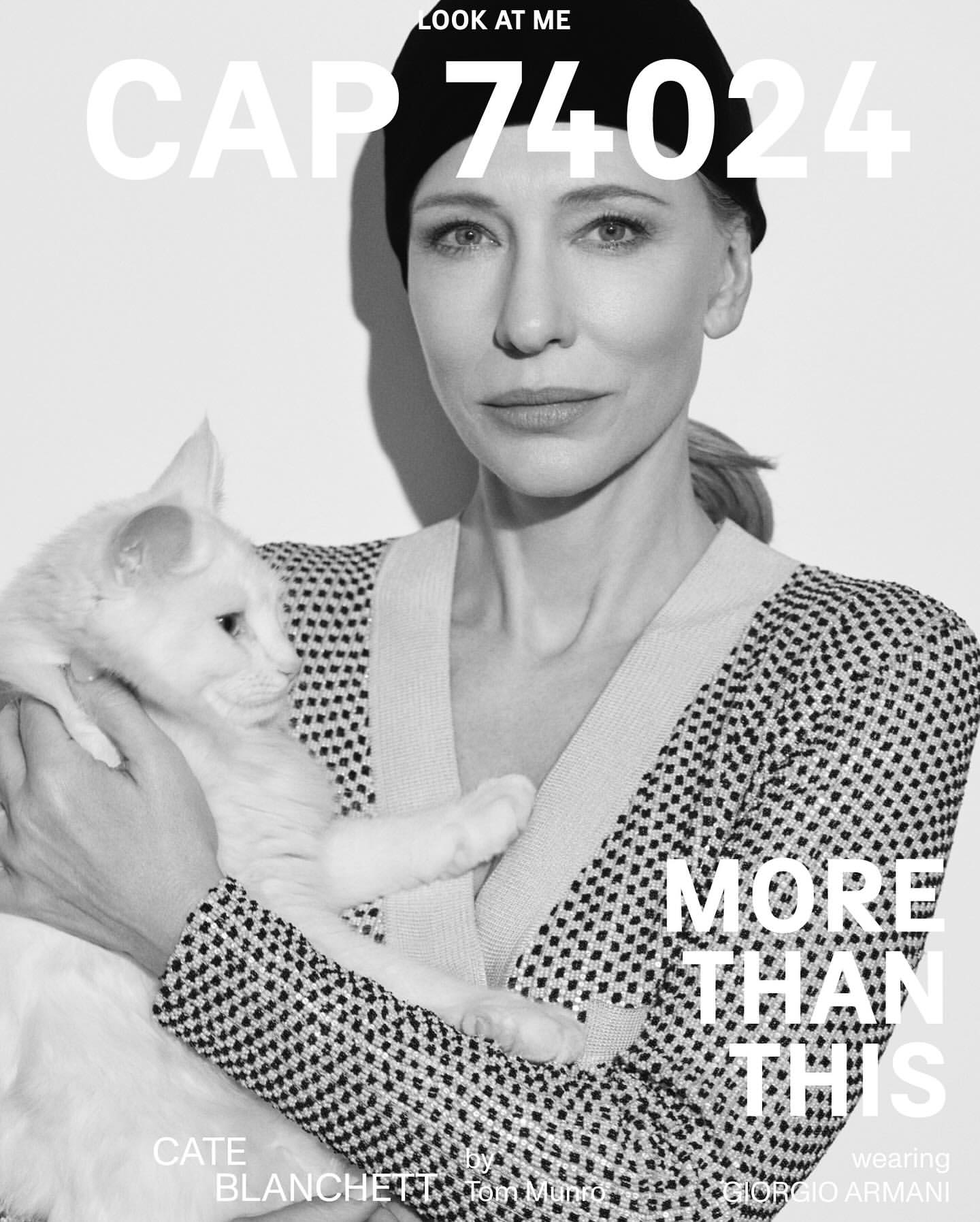 Black-and-white portrait of Cate Blanchett holding a white cat, wearing a patterned cardigan and black beanie, facing the camera.