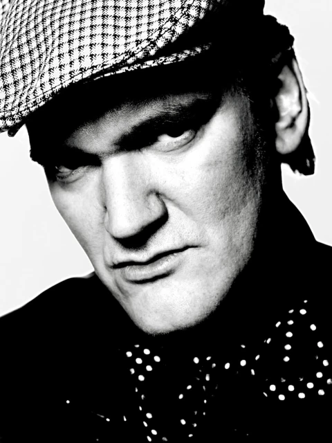 Monochrome portrait of an adult male wearing a newsboy cap and polka dot bow tie against a light background in a studio setting.