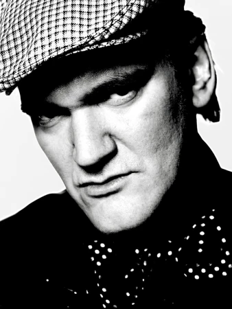 Monochrome portrait of an adult male wearing a newsboy cap and polka dot bow tie against a light background in a studio setting.
