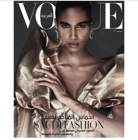 Vogue Arabia cover featuring a Black adult female model with gold eye shadow, wearing a shiny gold dress and diamond earrings in a studio.