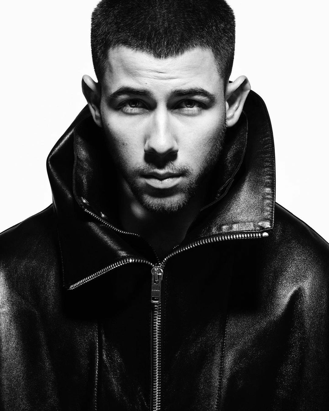 Black and white portrait of a man with short hair wearing a leather jacket, looking directly at the camera with a serious expression.