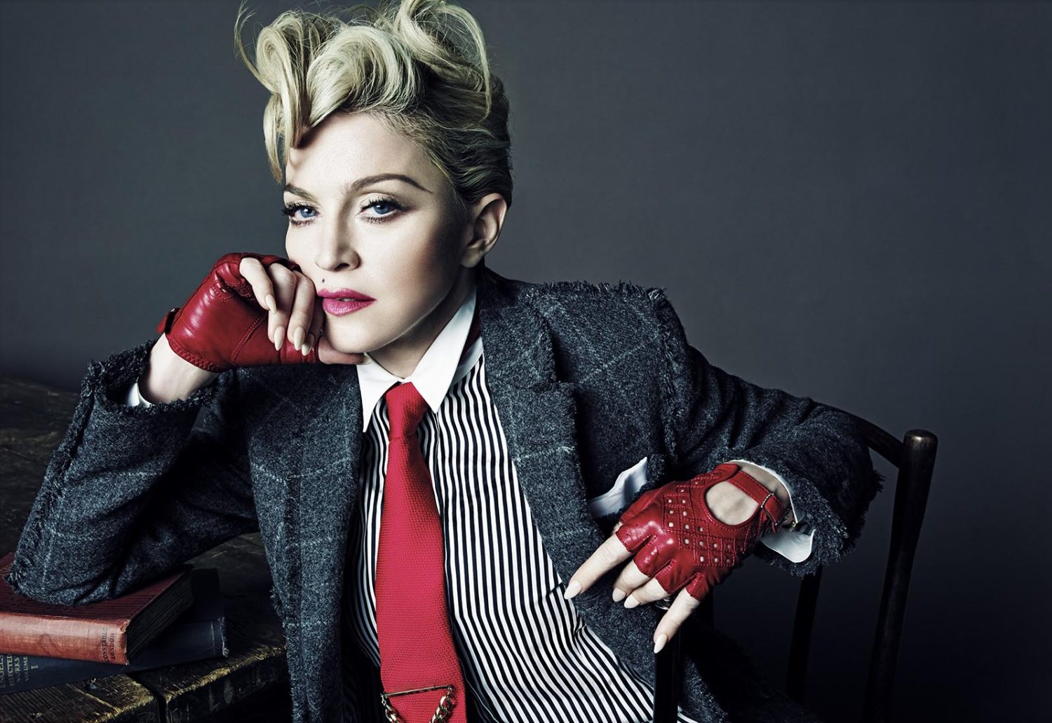 Madonna wearing a plaid suit jacket, vertical striped shirt, red tie, and red fingerless leather gloves