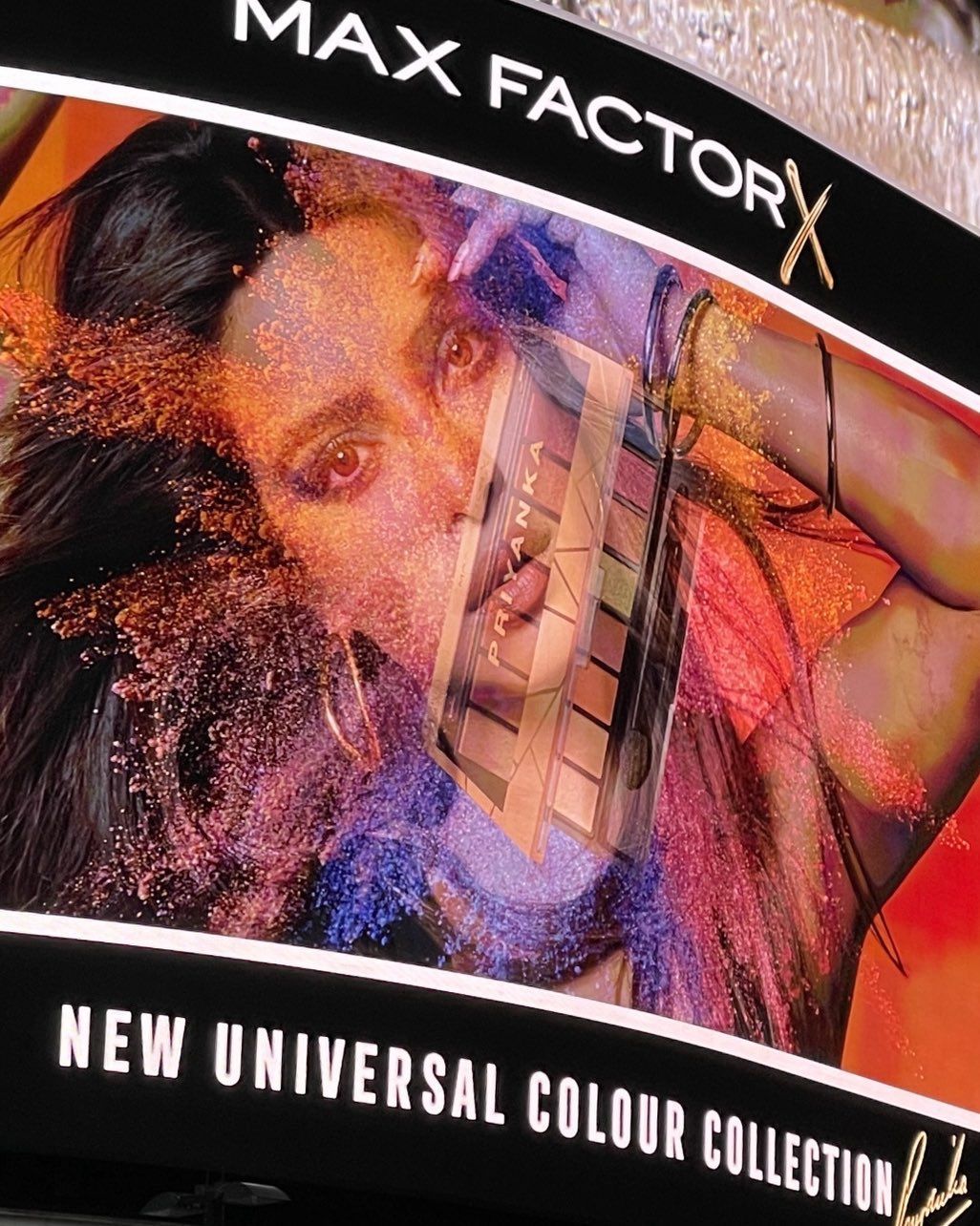 Cosmetics advertisement featuring a woman's face, makeup palette, and colorful powder explosion for Max Factor's Universal Colour Collection.