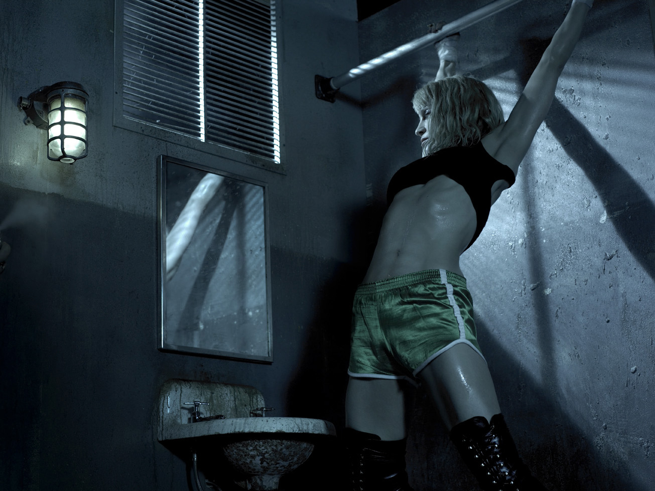 Athletic woman in green shorts and black boots leans against a wall in a grungy, dimly lit room with a sink, mirror, and barred window.
