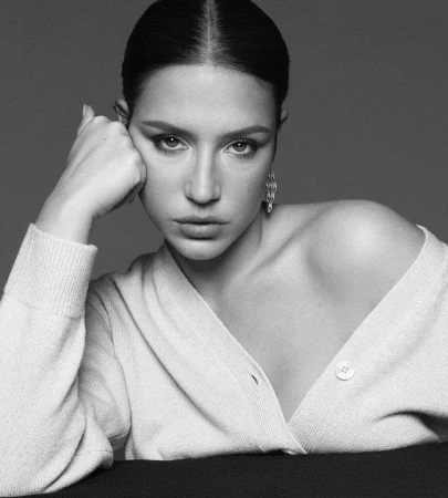 Monochrome portrait of a woman resting her head on her hand, wearing a knitted cardigan against a plain background