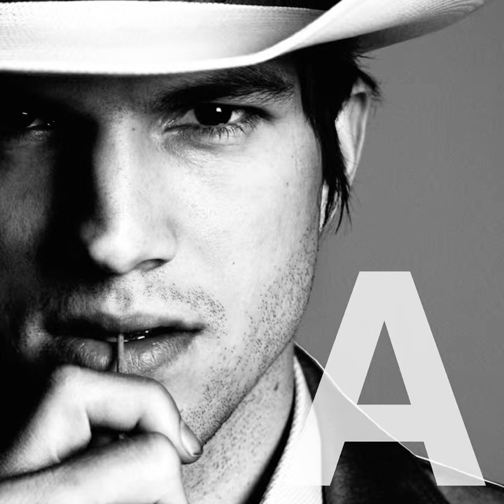 Monochrome portrait of an adult man with dark hair wearing a hat and a white shirt. The 'A' letter is superimposed on the image.
