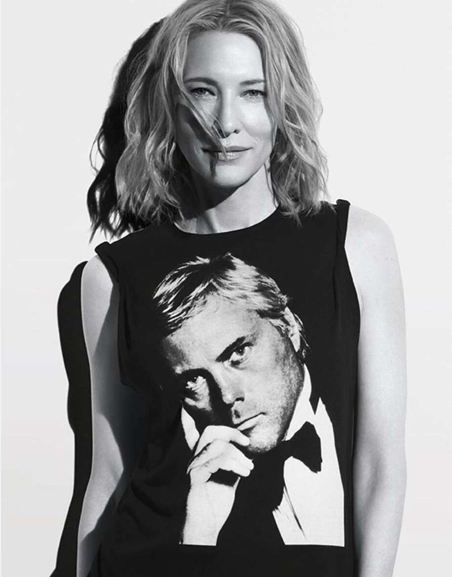 Black and white portrait of a woman with shoulder-length hair, wearing a shirt with a man's portrait on it against a white background.