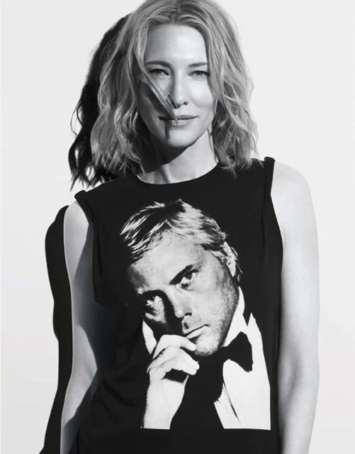Black and white portrait of a woman with shoulder-length hair, wearing a shirt with a man's portrait on it against a white background.