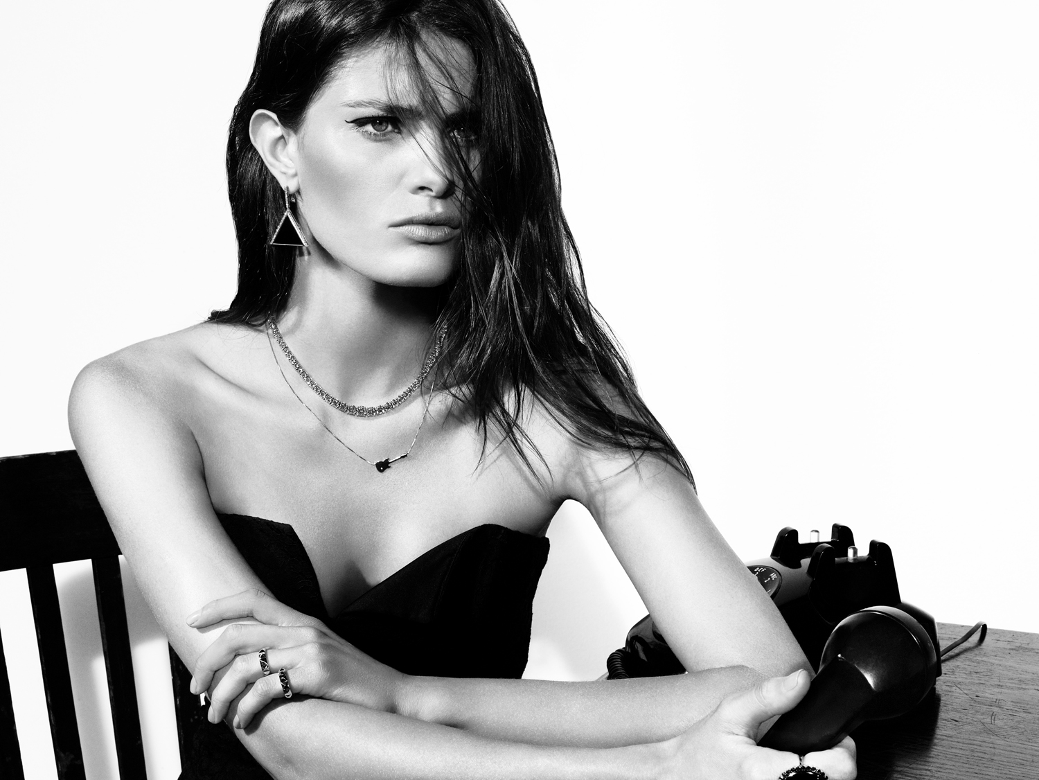 Monochrome portrait of a brunette woman wearing a strapless dress and layered necklaces, holding a rotary phone receiver.