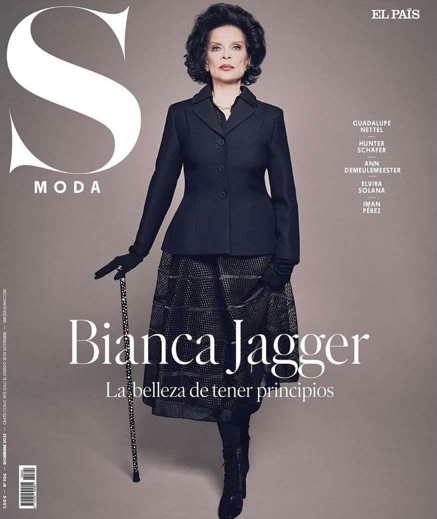 Bianca Jagger on El Pais S Moda magazine cover, wearing a dark jacket, patterned skirt, gloves, holding a cane, dark hair.