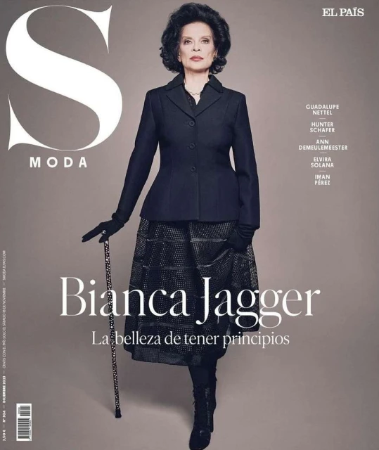 Bianca Jagger on El Pais S Moda magazine cover, wearing a dark jacket, patterned skirt, gloves, holding a cane, dark hair.