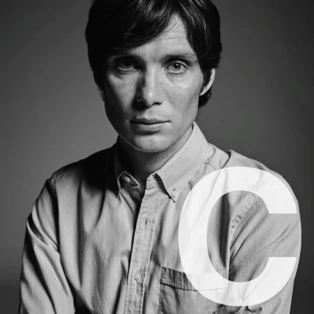 Black and white portrait of Cillian Murphy wearing a striped button-down shirt, captured in a close-up shot against a grey background.