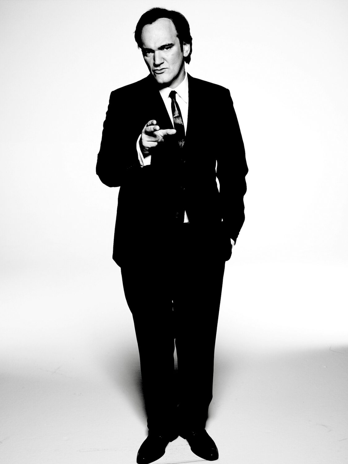 Portrait of a contemplative adult male with short brown hair, wearing a dark jacket and white t-shirt against a blurred background.