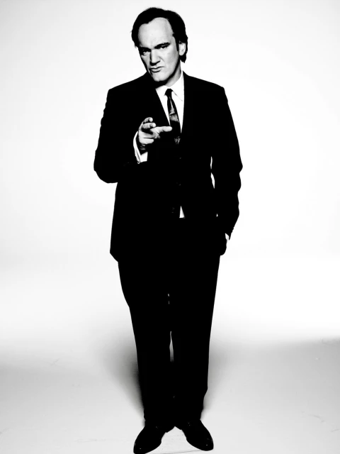 Portrait of a contemplative adult male with short brown hair, wearing a dark jacket and white t-shirt against a blurred background.