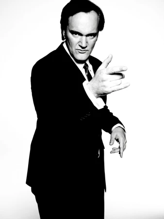 Monochrome portrait of Quentin Tarantino in a dark suit pointing toward the camera against a white seamless background.