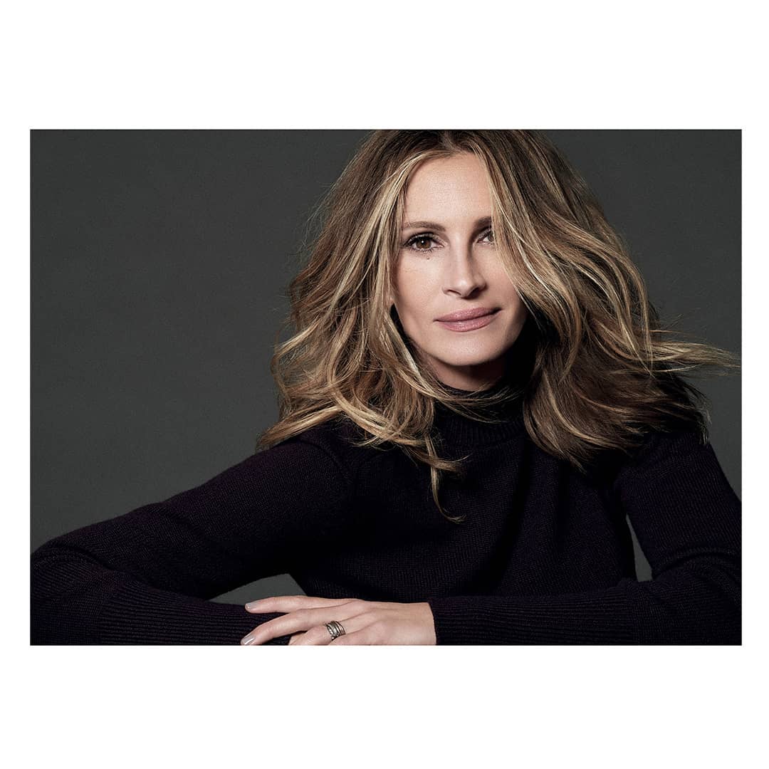Close-up studio portrait of Julia Roberts, showcasing her warm smile, and wavy blonde hair, wearing a black turtleneck sweater.