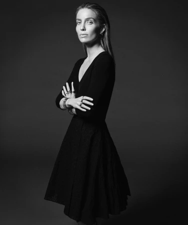 Black and white portrait of a woman with wet look hair standing with arms crossed wearing dark clothing