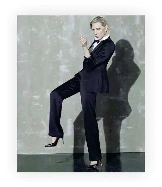 Elegant woman in a black suit and heels strikes a confident pose against a mottled grey backdrop, blending fashion and sophistication.