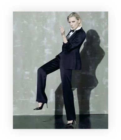 Elegant woman in a black suit and heels strikes a confident pose against a mottled grey backdrop, blending fashion and sophistication.