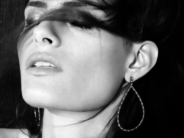 Close-up black and white portrait of a woman wearing a large teardrop earring with hair swept across her face by Tom Munro