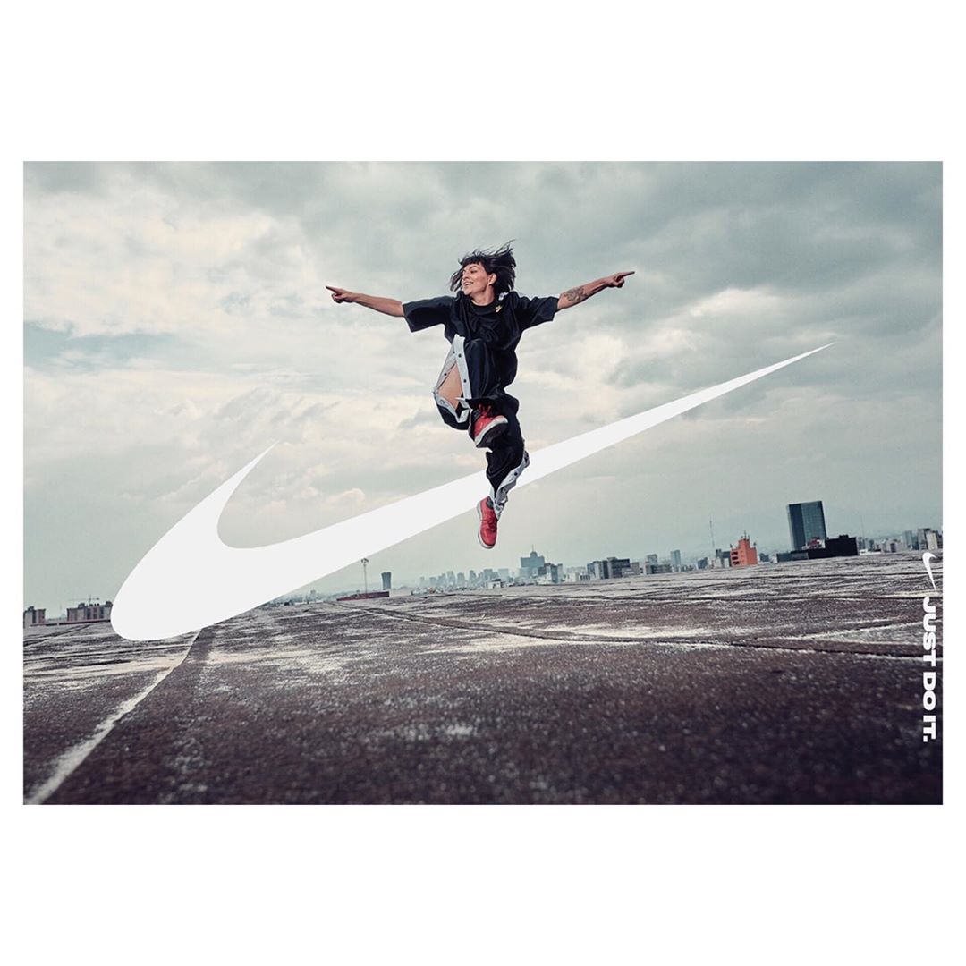 Athletic woman in motion jumping on a rooftop in athletic wear, sportswear, with a city skyline, cloudy sky and Nike swoosh.