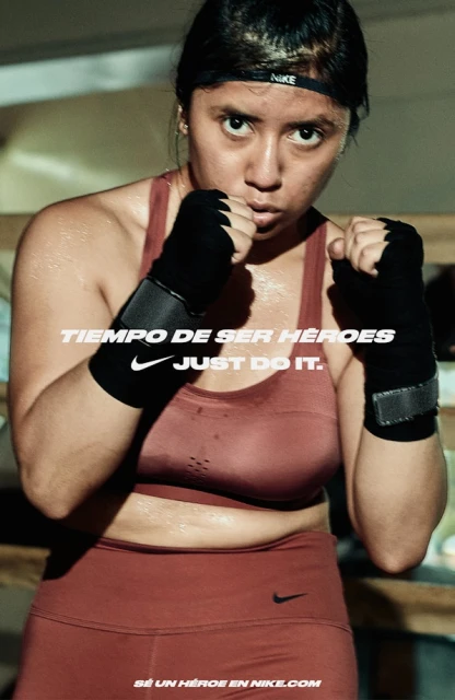 Portrait of a sweaty female athlete with boxing wraps on hands, wearing a sports bra and headband, advertising Nike athletic wear.
