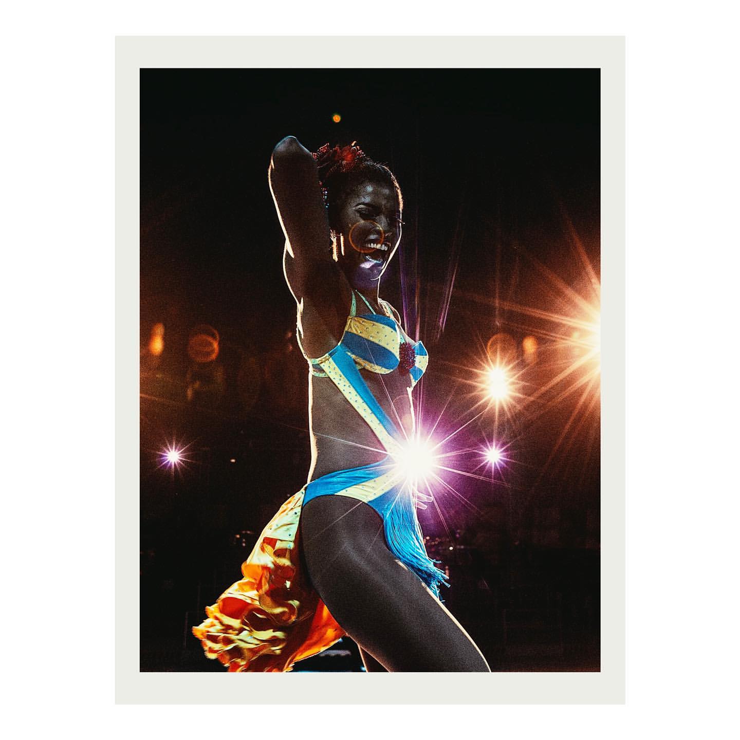 A joyful dark-skinned dancer with vibrant costume performs under bright stage lights, creating a lively and energetic visual spectacle.