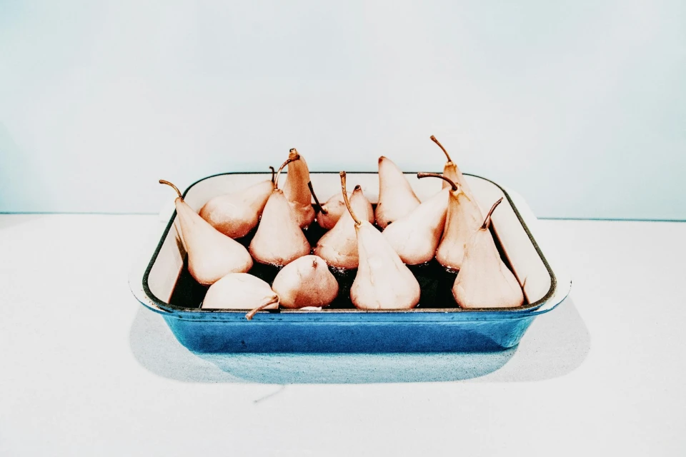 Poached pears in a blue baking dish against a white and light blue background, studio lighting, minimalist food still life.