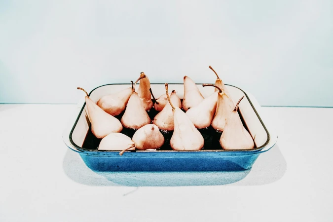 Poached pears in a blue baking dish against a white and light blue background, studio lighting, minimalist food still life.