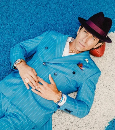 Man wearing a bright blue pinstripe suit and a dark fedora lying on a blue textured surface