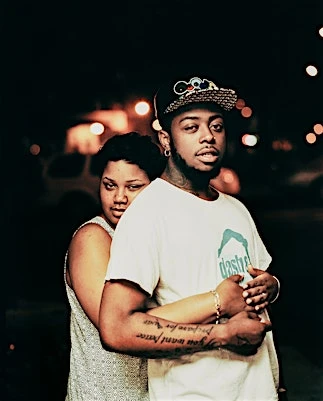 Portrait of a Black man and woman posing outdoors at night with soft bokeh lights in the dark background