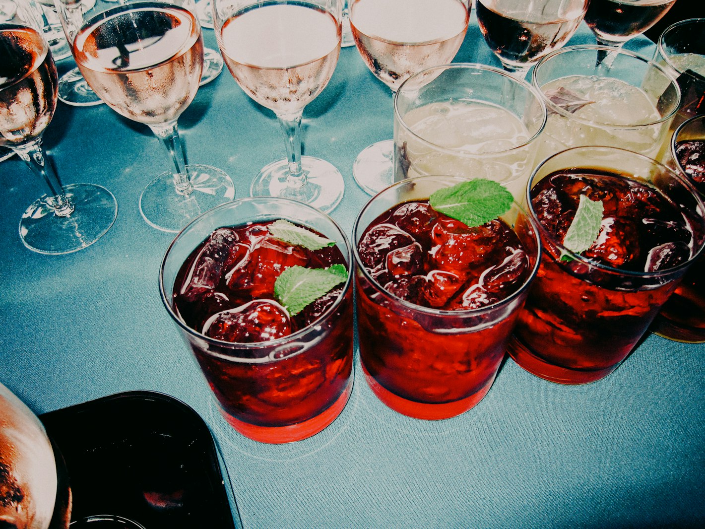 Several glasses of cocktails and wine are arranged on a blue surface, highlighting drinks, glassware, and a vibrant color palette.