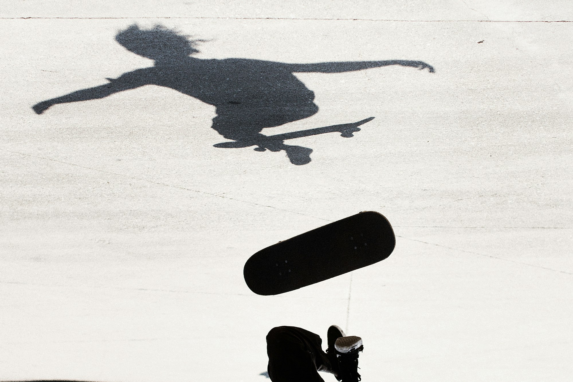 Silhouette of a skateboarder captured mid-air during a trick, with a focus on the form against a bright background.