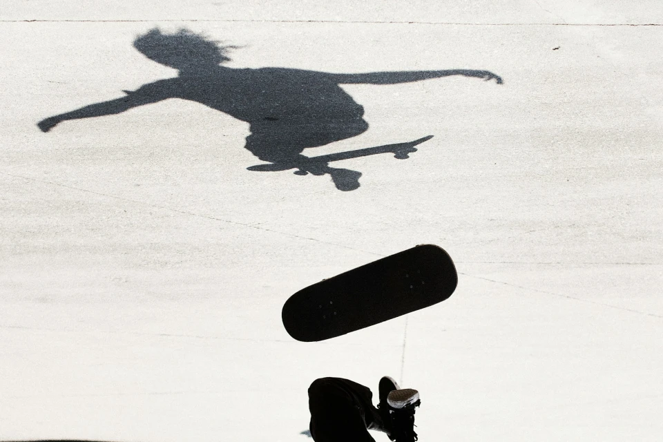 Silhouette of a skateboarder captured mid-air during a trick, with a focus on the form against a bright background.