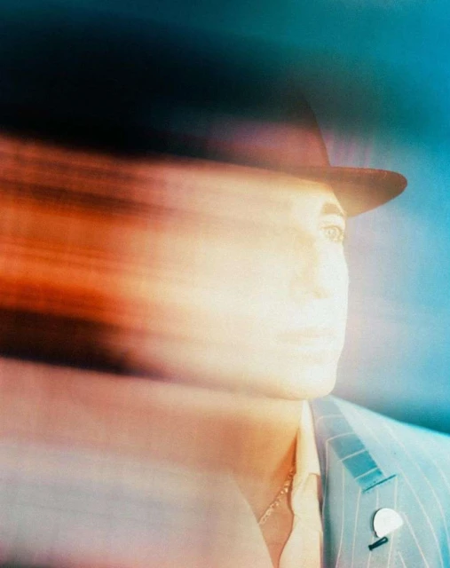 An abstract portrait of a person wearing a hat and suit jacket, created with intentional motion blur and rendered in shades of orange and blue.