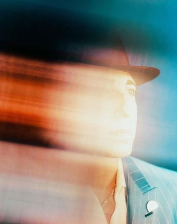 An abstract portrait of a person wearing a hat and suit jacket, created with intentional motion blur and rendered in shades of orange and blue.