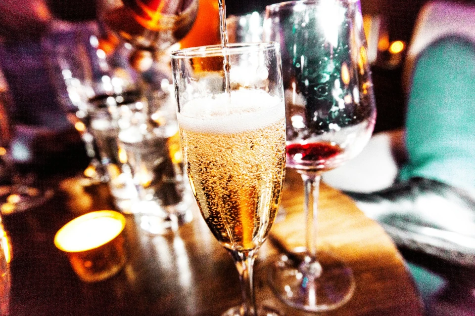 Champagne is poured into a flute glass, accompanied by a candle and red wine in a glass, all resting on a wooden table.
