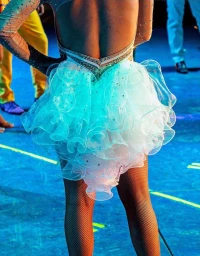 Close-up back view of a performer wearing a white ruffled dance costume with sheer sleeves and fishnet tights on a blue lit stage.