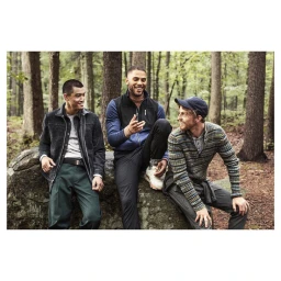 Three men smiling and laughing together while sitting on a large rock in a forest outdoors, captured by Christaan Felber.